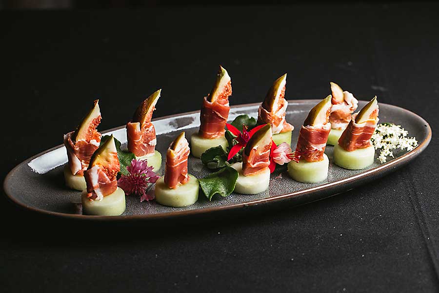 Canapes on the oval plate, cucumber base topped with passionfruit and hickory smoked bacon