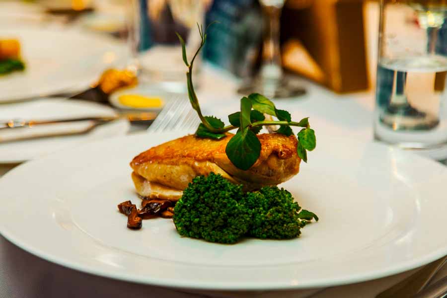 Chef Robert Morales presenting a crusted chicken breast, broccolini, edible micro herbs, field mushrooms soil