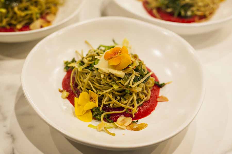 Chef Valeria Boselli presenting Vegan edamame pasta with edible flowers, toasted almonds, beetroot puree