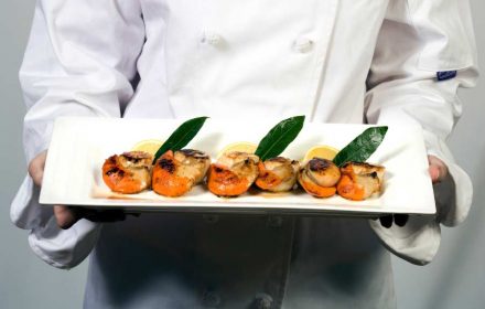 a male chef is presenting a plate of BBQ scallops with roe