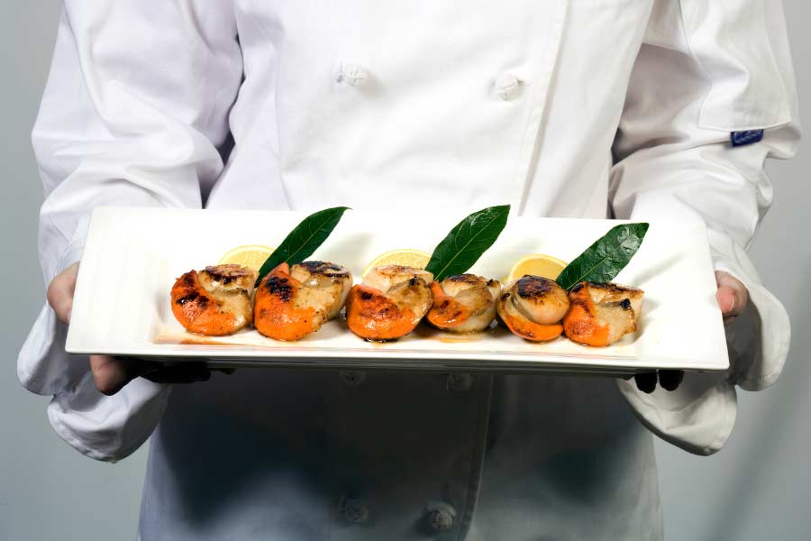 a male chef is presenting a plate of BBQ scallops with roe