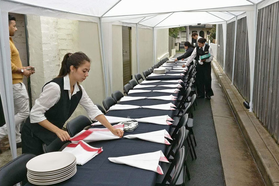 a staff team setting up a laneway dining table under a tent in a rainy day